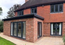 Anthracite grey aluminium bi-fold doors opening onto a patio from a modern brick extension