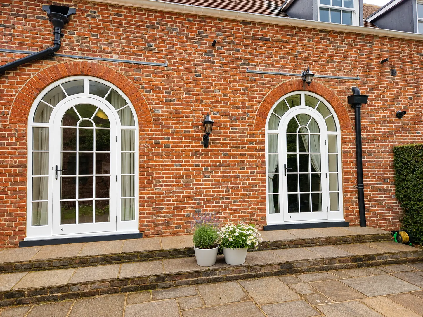 Pair of white arched French doors with astragal bars set into red brick openings on a period property
