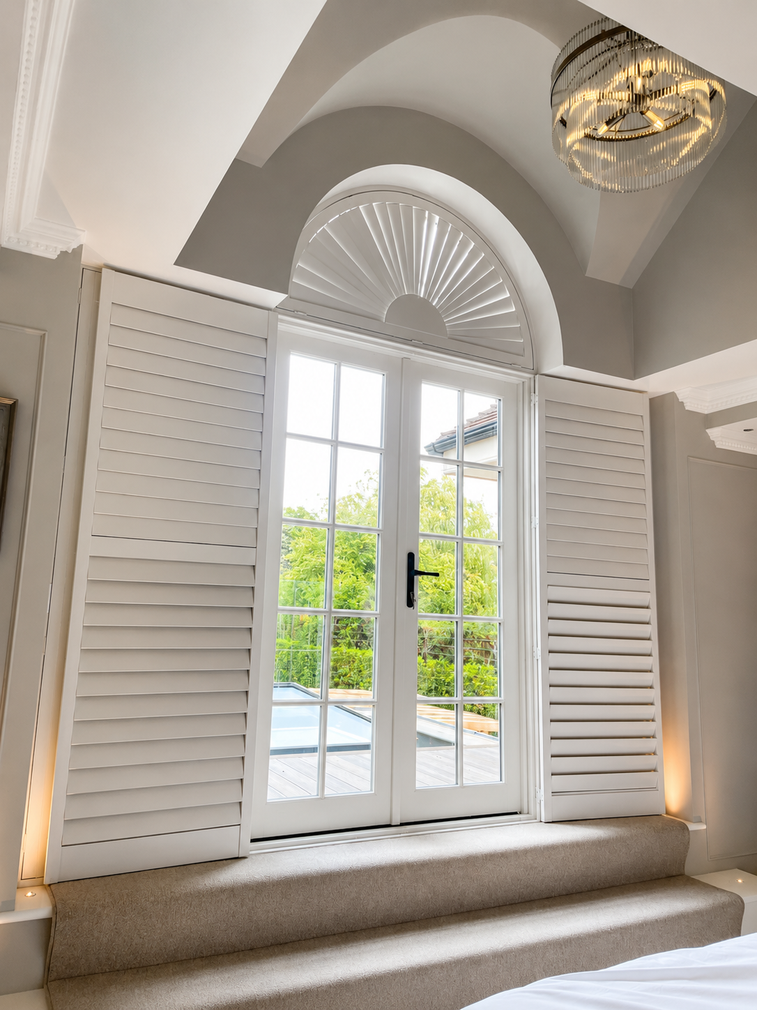 Interior view of white arched French doors with a fanlight and plantation shutters in a bedroom